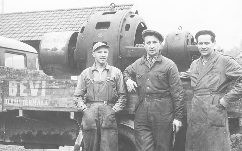 Kolme miestä työvaatteissa kuorma-autolla, jossa oli suuri sähkömoottori tasossa, noin 1940.
